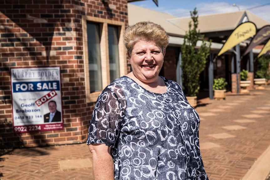 A woman standing in front of a building with a sold sticker on a real estate sign.