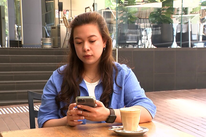 a young woman sitting  by herself at a table looking at her mobile phone