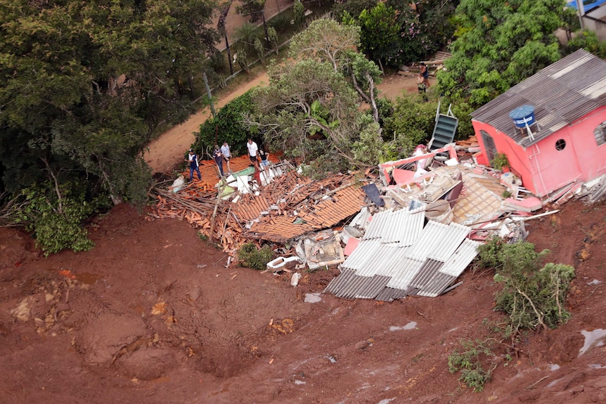 An aerial view shows a destroyed house surrounded by mud after a dam collapse.