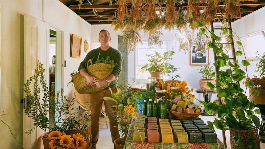 Richard Christansen stands in sunny yellow room filled with fliowers, soap and baskets of fruit