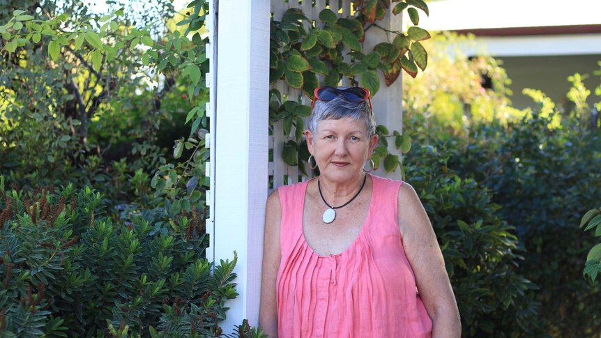 A middle-aged woman stands in the garden in front of her home