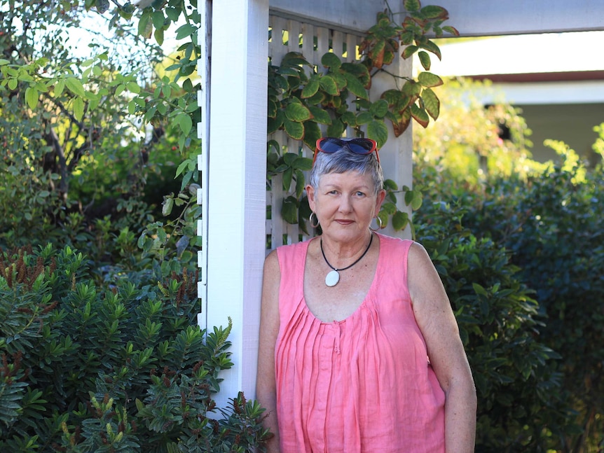 A middle-aged woman stands in the garden in front of her home