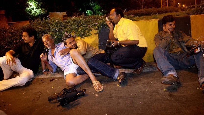Indian men, along with journalists, take cover at one of the attack sites in Mumbai
