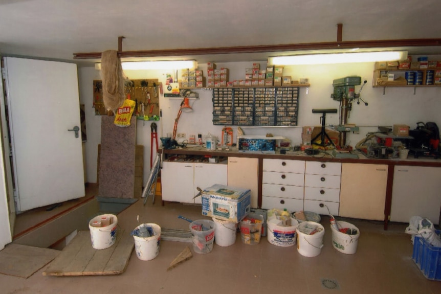 A workshop with tools on a bench and open plastic buckets on the floor.