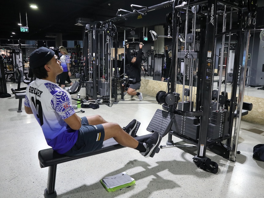 A young man pictured side on pulling weights in a seated position