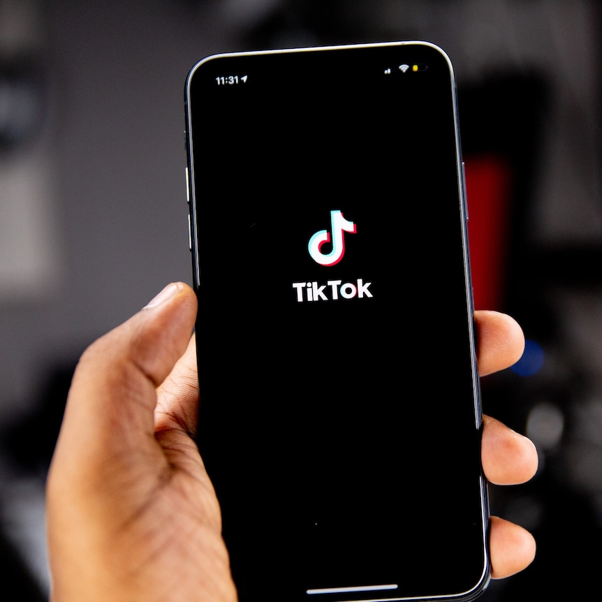 A person's hand holding an iPhone, which is displaying the TikTok logo