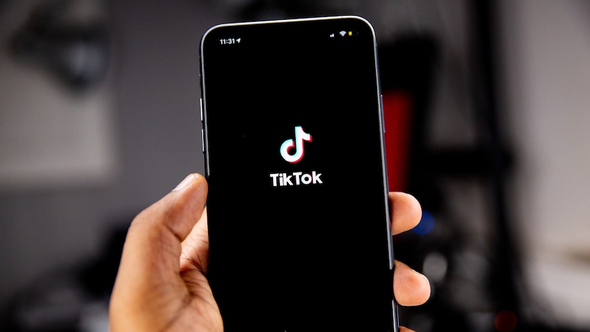 A person's hand holding an iPhone, which is displaying the TikTok logo