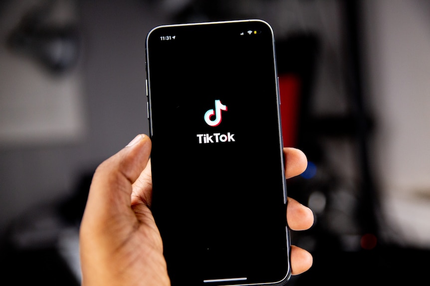 A person's hand holding an iPhone, which is displaying the TikTok logo