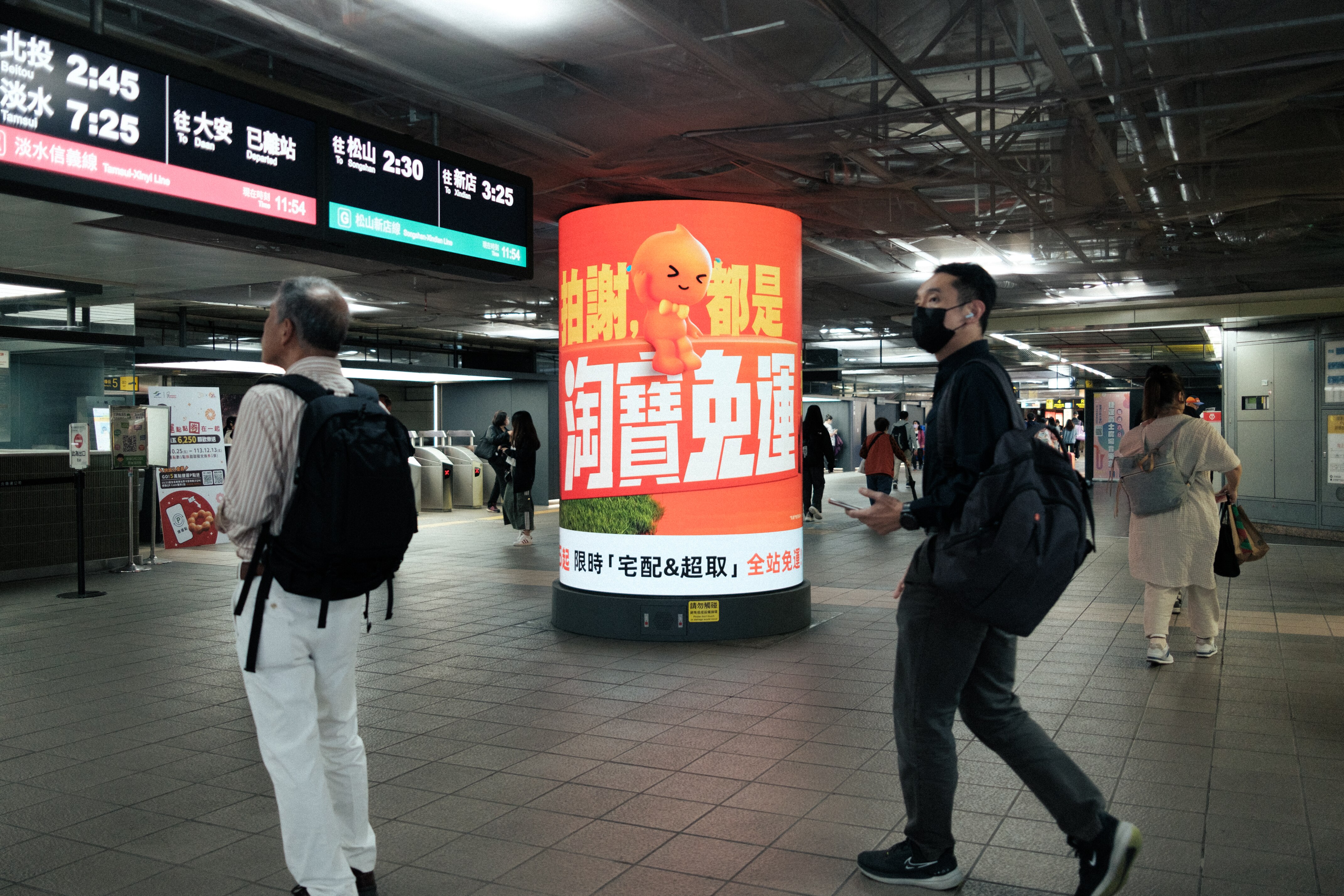 A man walking in front of a banner with advertisement in Chinese characters. 