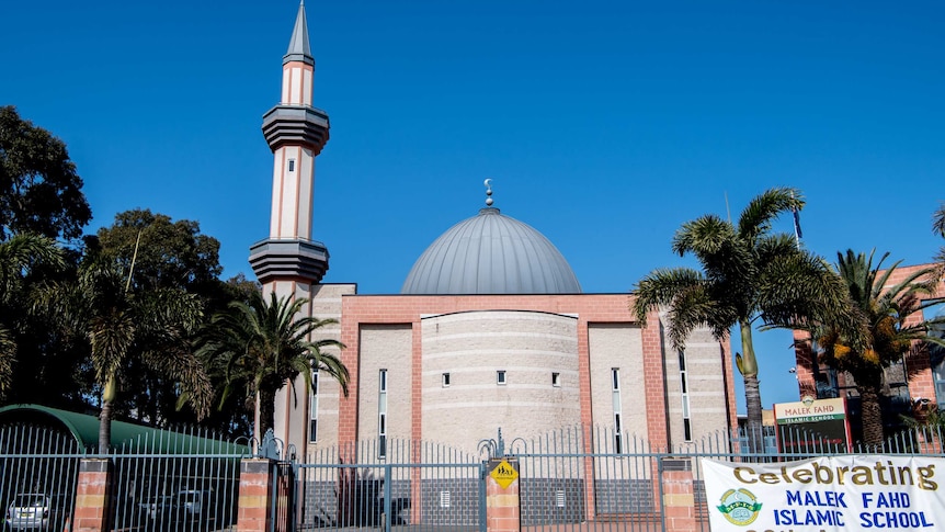 A school with a dome roof is surrounded by palm trees.