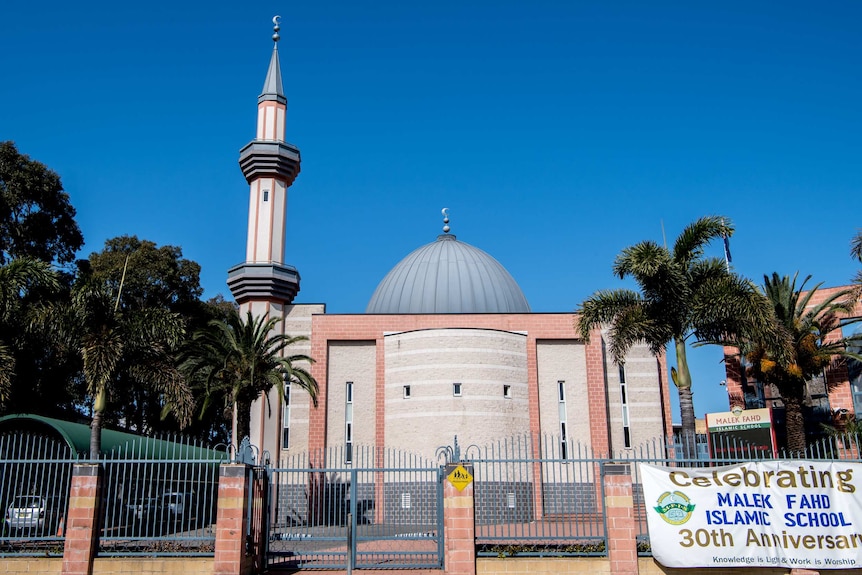 A school with a dome roof is surrounded by palm trees.