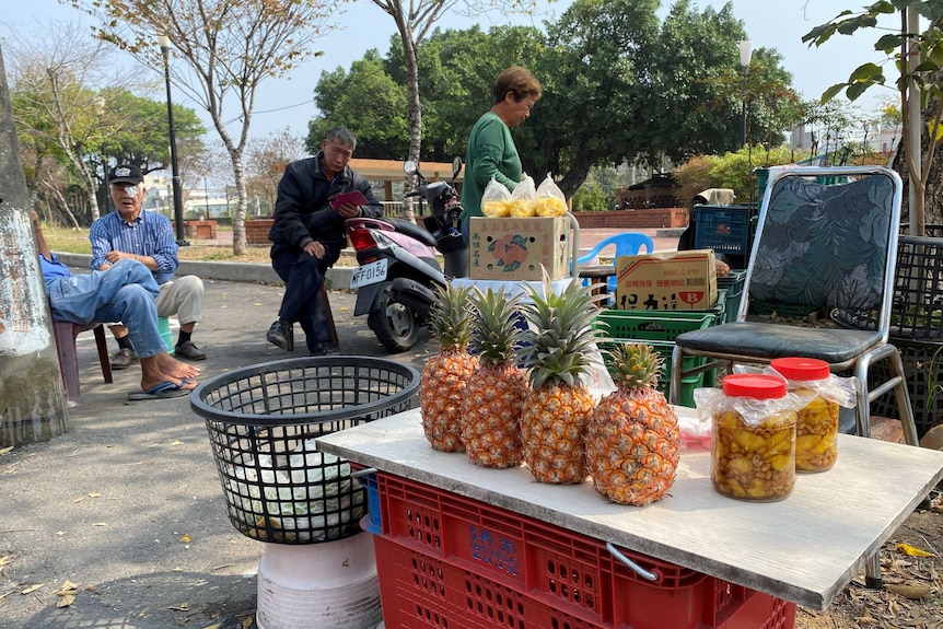 Some fresh and bottled pineapples sit on a table with old people sitting around.