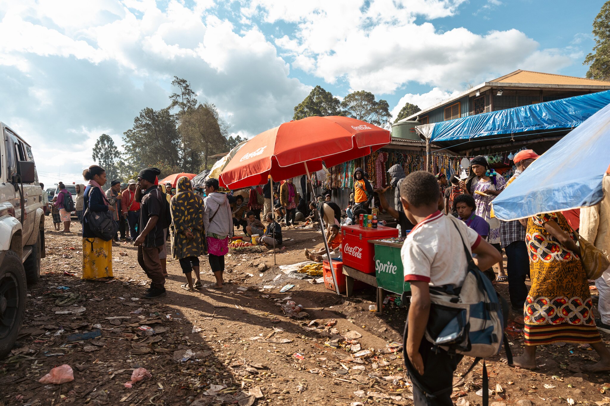 People walk past roadside stalls selling coca cola and sprite, on a dirt road