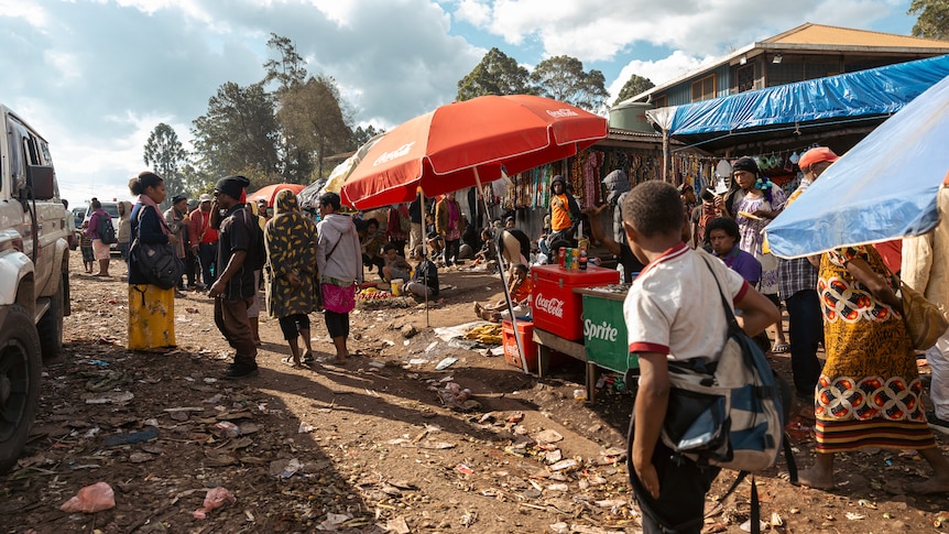 People walk past roadside stalls selling coca cola and sprite, on a dirt road