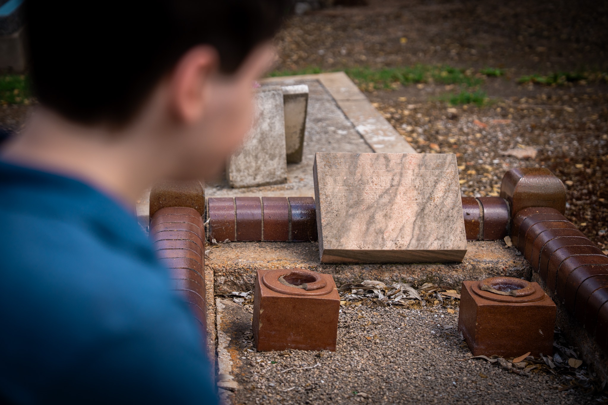Blurry image of a young man in blue shirt looking at a gravesite
