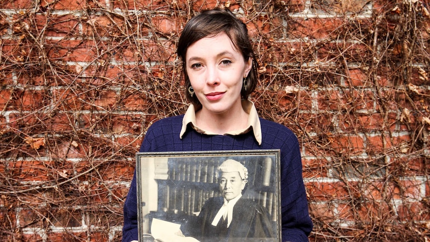 Young woman holds a portrait of her relative in barrister attire.