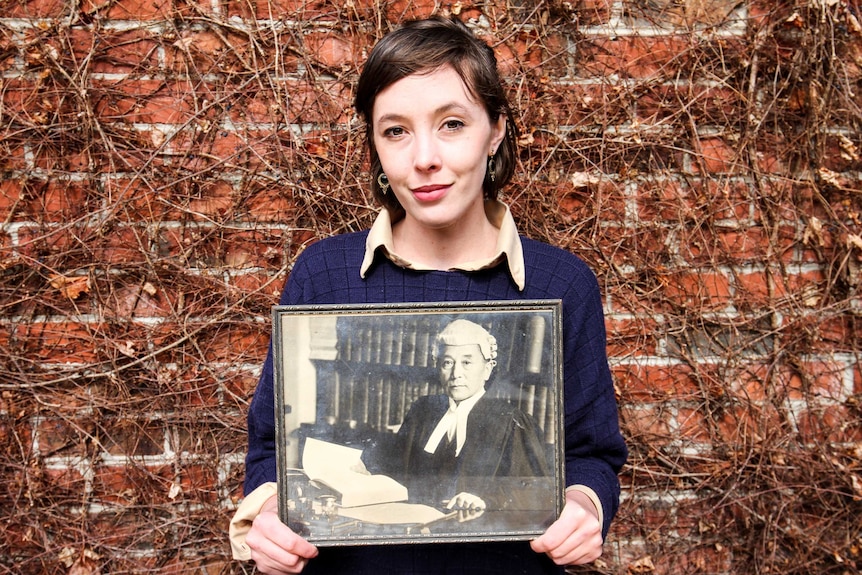 Young woman holds a portrait of her relative in barrister attire.