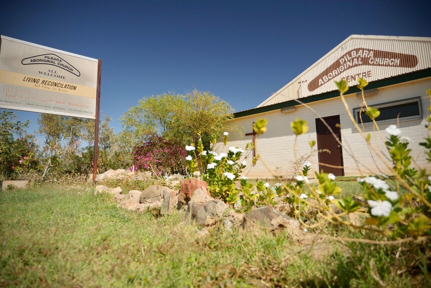 Corrugated iron building of the Pilbara Aboriginal Church in the background, with flower garden in foreground