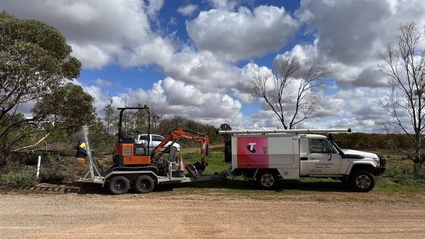 A Telstra van towing an excavator. 