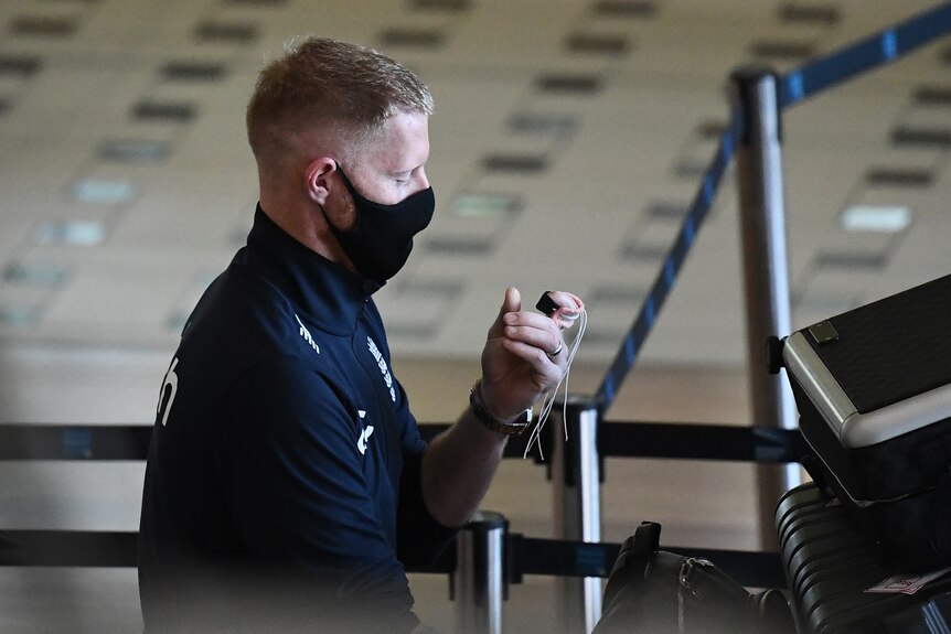 England's Ben Stokes walks through Brisbane Airport looking at a thick medical bandage wrapped around his finger. 