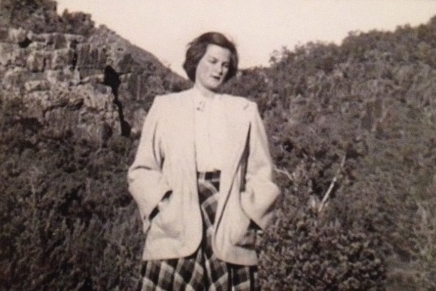 black and white image of a woman in a checkered skirt and jacket with mountains behind