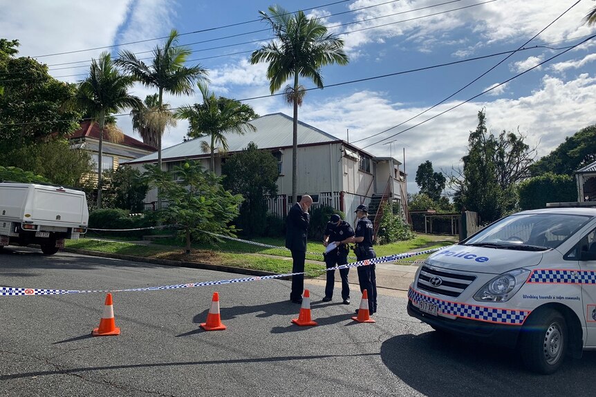 Three police officers stand outside a home in Annerley, with police tape surrounding the crime scene.
