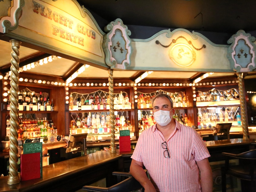 A wide shot of David Heaton standing in his brightly colored bar wearing a pink business shirt