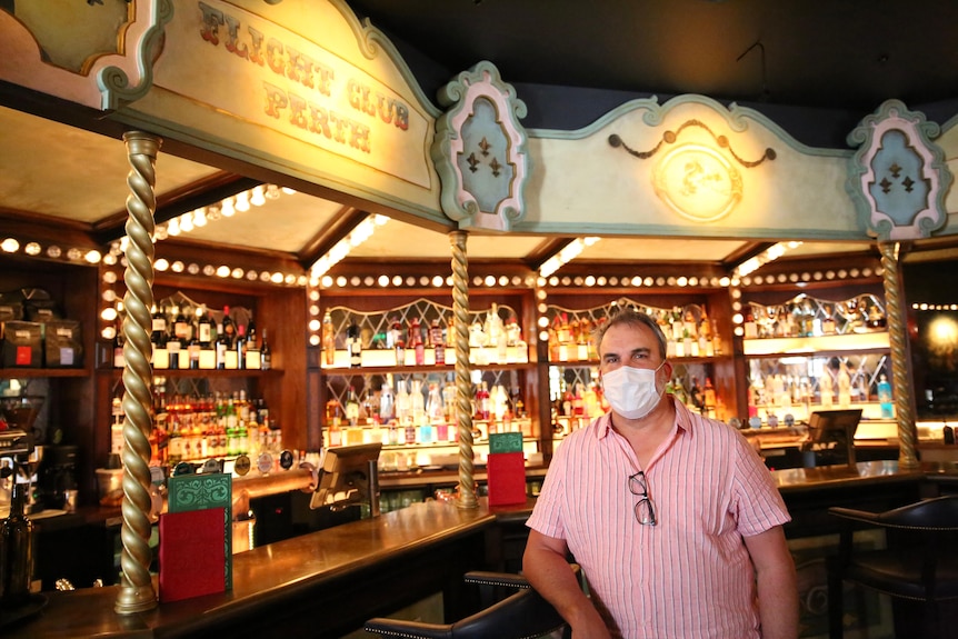 A wide shot of David Heaton standing in his brightly colored bar wearing a pink business shirt