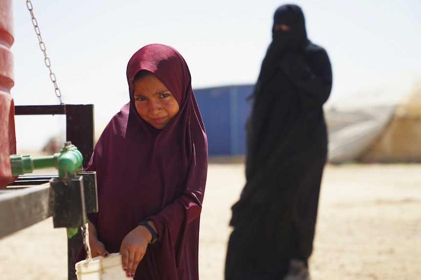 Maysa Assad collecting water from a water tank in the al-Hawl camp in Syria, wearing a maroon hijab.