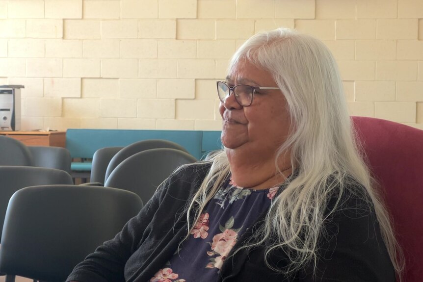 An Aboriginal woman with long white hair and glasses sitting on a couch.