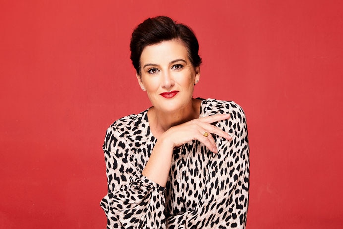 Portrait of a middle-aged woman with short brown hair and red lipstick against a red background.