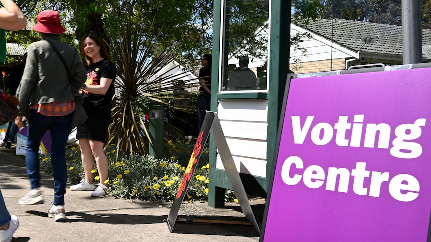 Three people walking at a polling station, with a sign which reads voting centre