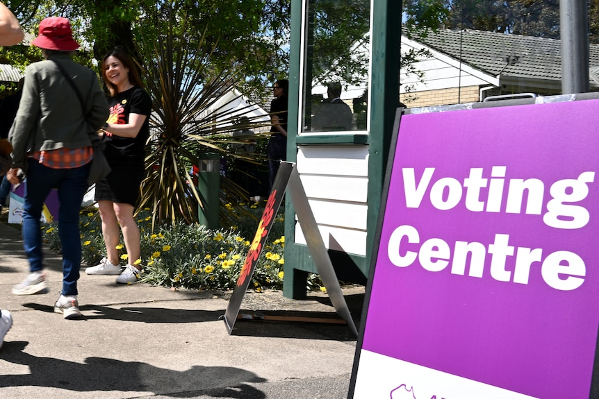 Three people walking at a polling station, with a sign which reads voting centre