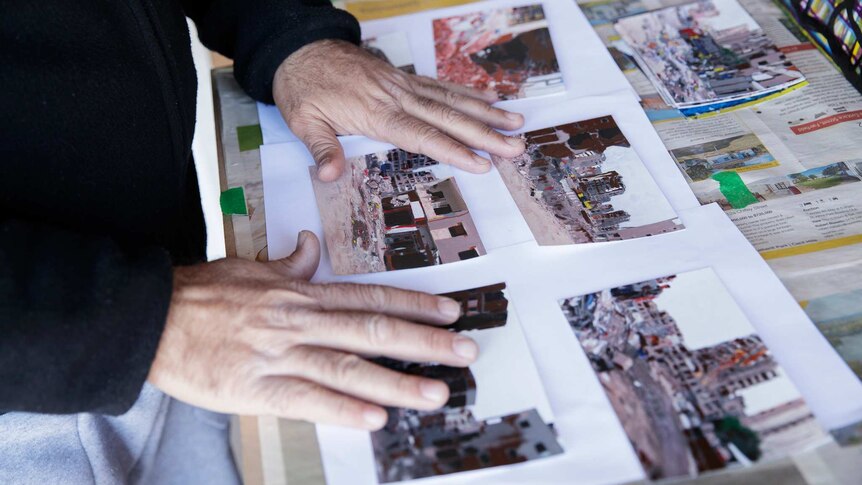 Artist's hands laying out several small photo prints of a bombed cityscape, laid on top of a white sheet of paper and newspaper.