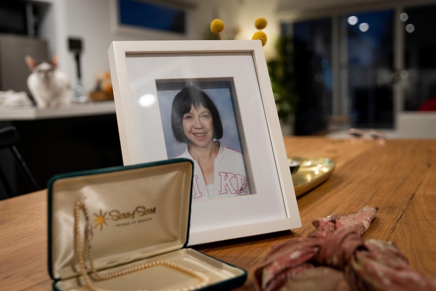 A photograph of a woman with dark hair sits beside an open jewellery box containing a pearl necklace. 