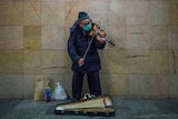 An old man playing the violin in a surgical face mask