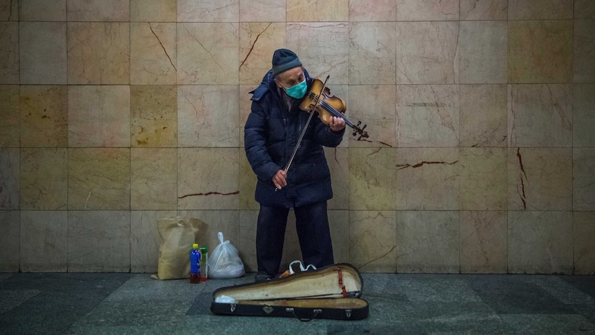 An old man playing the violin in a surgical face mask