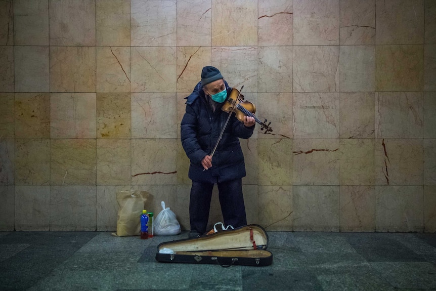 An old man playing the violin in a surgical face mask