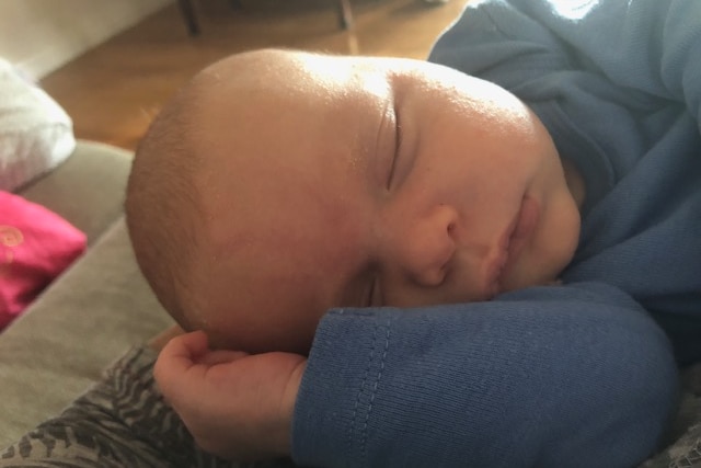 A close up image of a baby sleeping, his eyes are closed and he is lying on one arm.