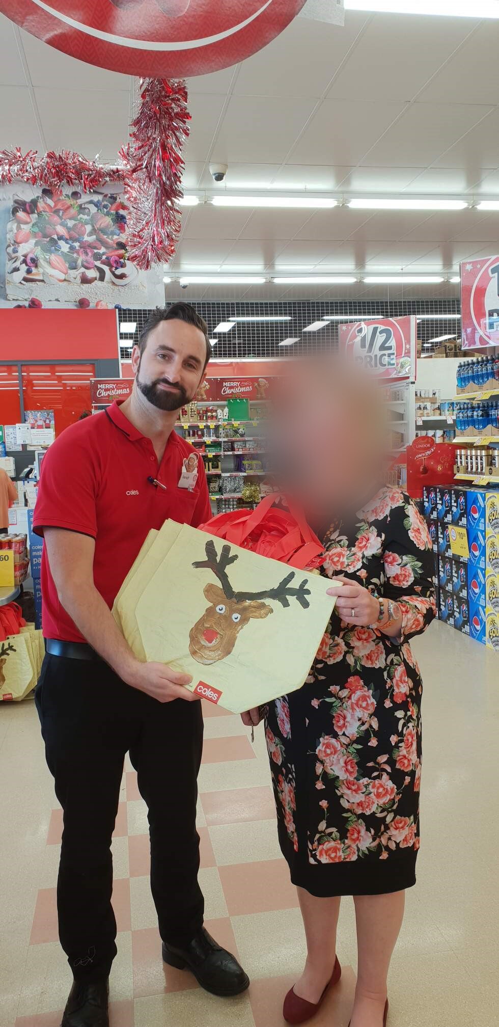 Darah presents a bag with a reindeer on it to a female Coles customer whose face is blurred.