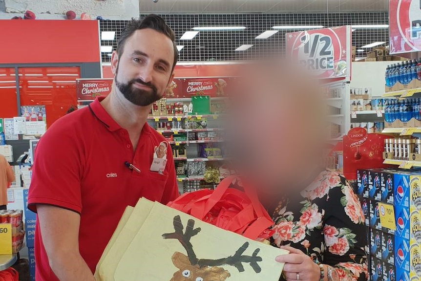 Darah presents a bag with a reindeer on it to a female Coles customer whose face is blurred.