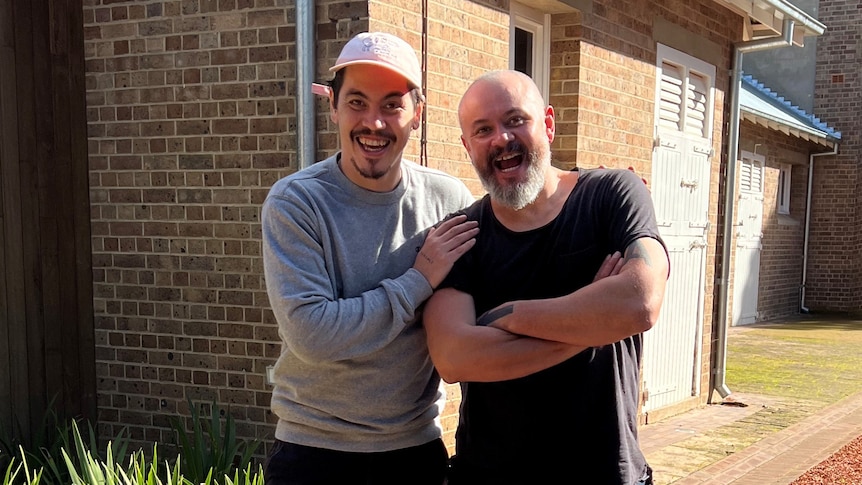 The brothers stand outside a home, laughing and looking relaxed in each other's company.  