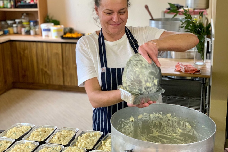 A woman dishes up macaroni and cheese into takeaway dishes.