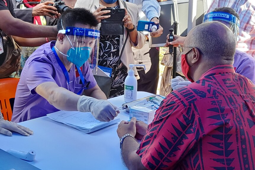 A Chinese nurse in a face shield hands a pen to a Papua New Guinean man