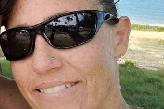 A close-up  photo of a smiling woman wearing black sunglasses at a beach