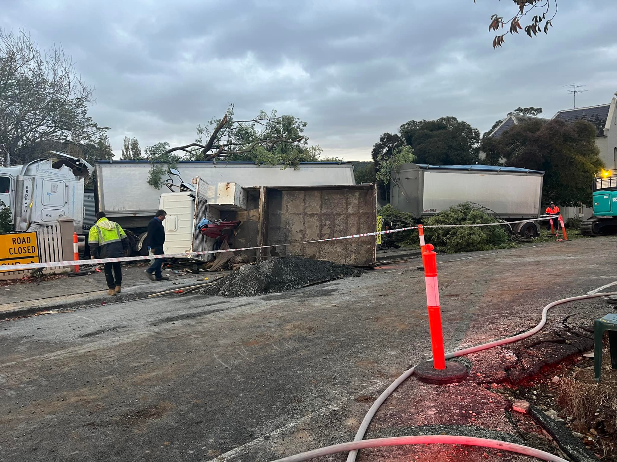 A tipper truck on its side in front of a larger B-double truck.