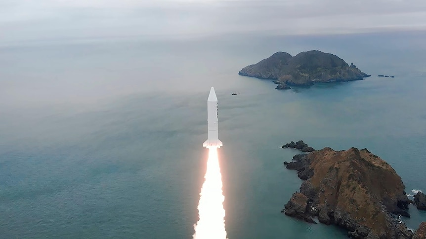 White rocket being launched near ocean.