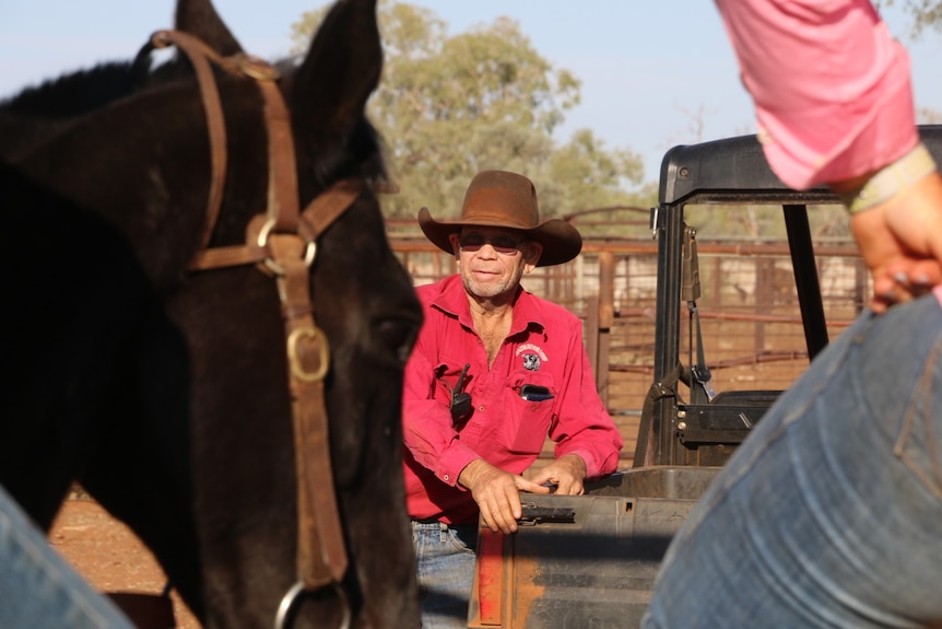 Dennis wearing a bright red shirt looking up at people on horses.