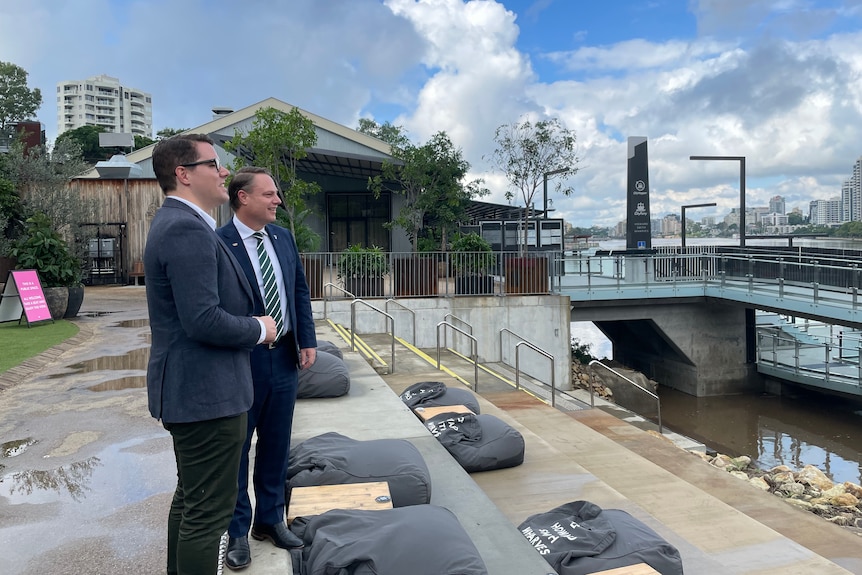 Two white men in jackets look at city river