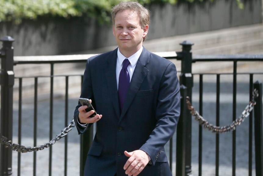 Grant Shapps holds his mobile phone as he walks through the Parliamentary Estate.